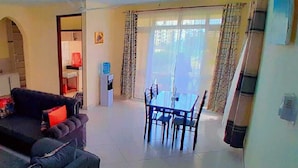 A living room with a sofa, a small table, and a dining area with a table and chairs. - Lux Suites Concord Apartments Mtwapa (Mtwapa)