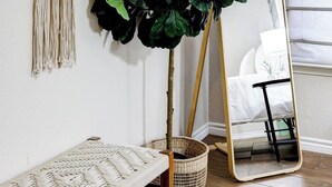 Ein Zimmer mit einer Bank, einem großen Topfpflanzen, einem Spiegel und einer Wanddekoration aus Makramee.