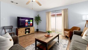 A living room with a flat-screen TV, a ceiling fan, a wooden coffee table, a sofa, a chair, and a potted plant. - 8 mi Lackland AFB BMT HotTub Game Room Bocce Ball (San Antonio)