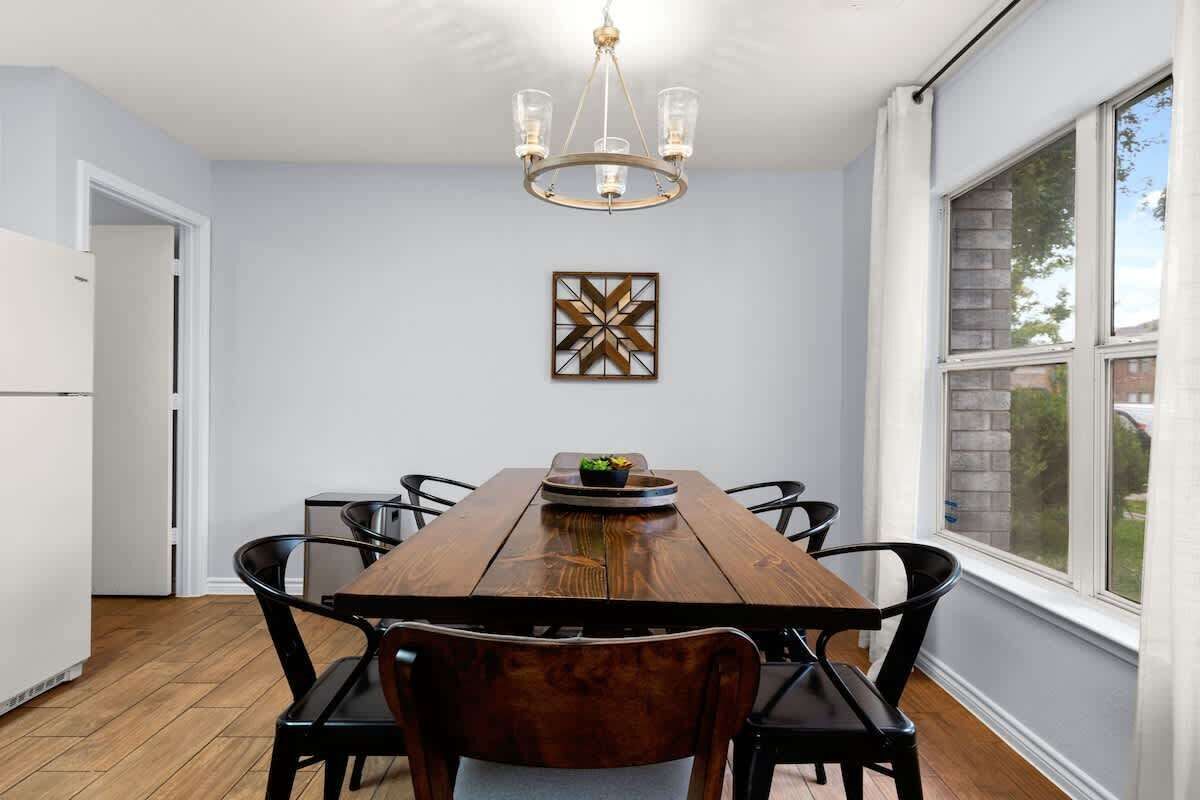 A dining area with a wooden table, black chairs, a chandelier, and a window with a view.