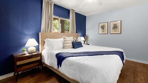 A bedroom with a bed, nightstand, lamp, ceiling fan, window with curtains, and two framed pictures on the wall. - 8 mi Lackland AFB BMT HotTub Game Room Bocce Ball (San Antonio)