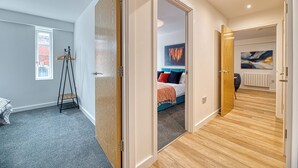 A modern bedroom with a bed, a standing lamp, and a view into another room. - Alexandra House by Guestz (Stockport)