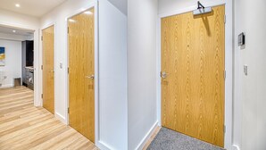 A hallway with wooden doors, a kitchen area, and a gray carpet leading to a door. - Alexandra House by Guestz (Stockport)