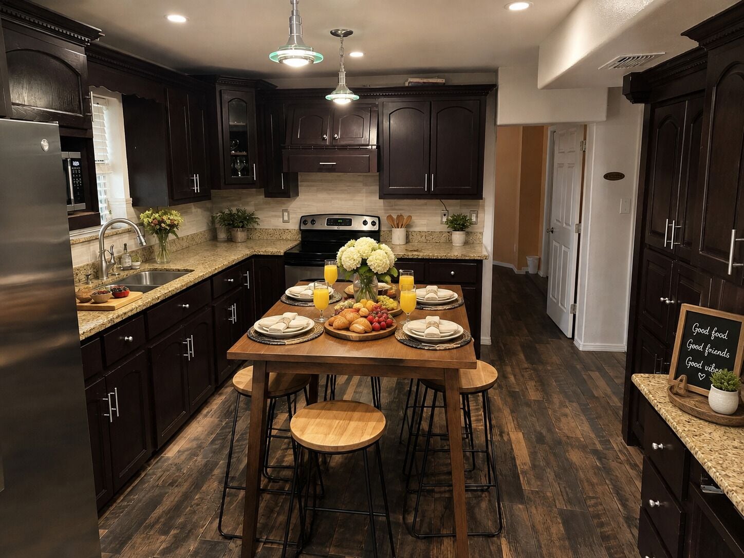 A modern kitchen with dark wood cabinets, a granite countertop, and a dining area set with stools.