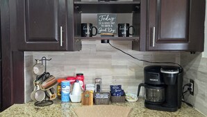 A kitchen with dark wood cabinets, a coffee maker, and various kitchen items on the counter. - 5BR retreat/Sleeps large groups/Spacious backyard/Near South Padre and Space X. (Brownsville)