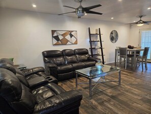 A living room with a leather sofa, a glass coffee table, a ladder, and a dining area with chairs and a table.