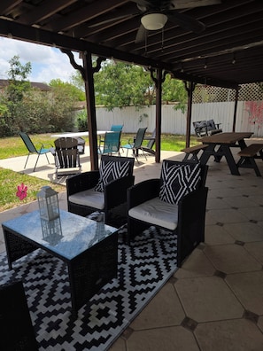Une terrasse extérieure aménagée avec des meubles en osier, une table en verre et un tapis à motifs.