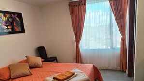 A bedroom with a bed, pillows, a chair, a painting, and curtains.