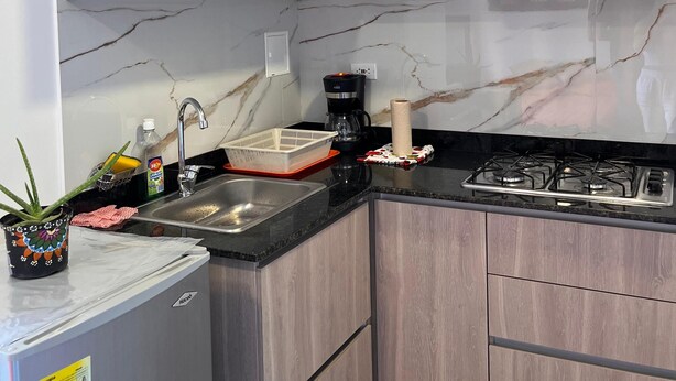 A kitchen with wooden cabinets, a marble backsplash, a refrigerator, a coffee maker, and a gas stove.