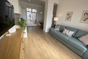 A modern living room with a wooden floor, a sofa, a TV, and a dining area in the background. - Travel Habitat Bioparc with Terrace Apartment A (Valencia)