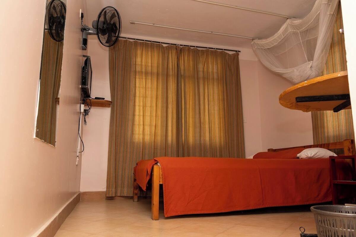 A room with a bed, a fan, a curtain, and a small table.