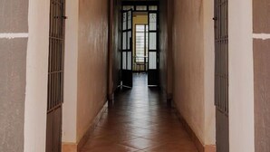 Un pasillo con piso de baldosas, una puerta al final y ventanas con barrotes en las paredes.