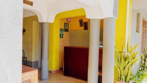 Un pasillo con paredes amarillas, columnas blancas y una puerta roja. Hay un letrero que dice 'Karibu Welcome'.