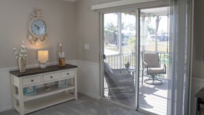 Ein Zimmer mit einer Schiebeglastür, die auf einen Balkon führt, einem weißen Schminktisch mit Schubladen, einer Wanduhr und einem Blumentopf.