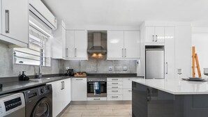 A modern kitchen with white cabinetry, a built-in oven, a stainless steel refrigerator, and a washing machine. - Sea La Vie (Cape Town)