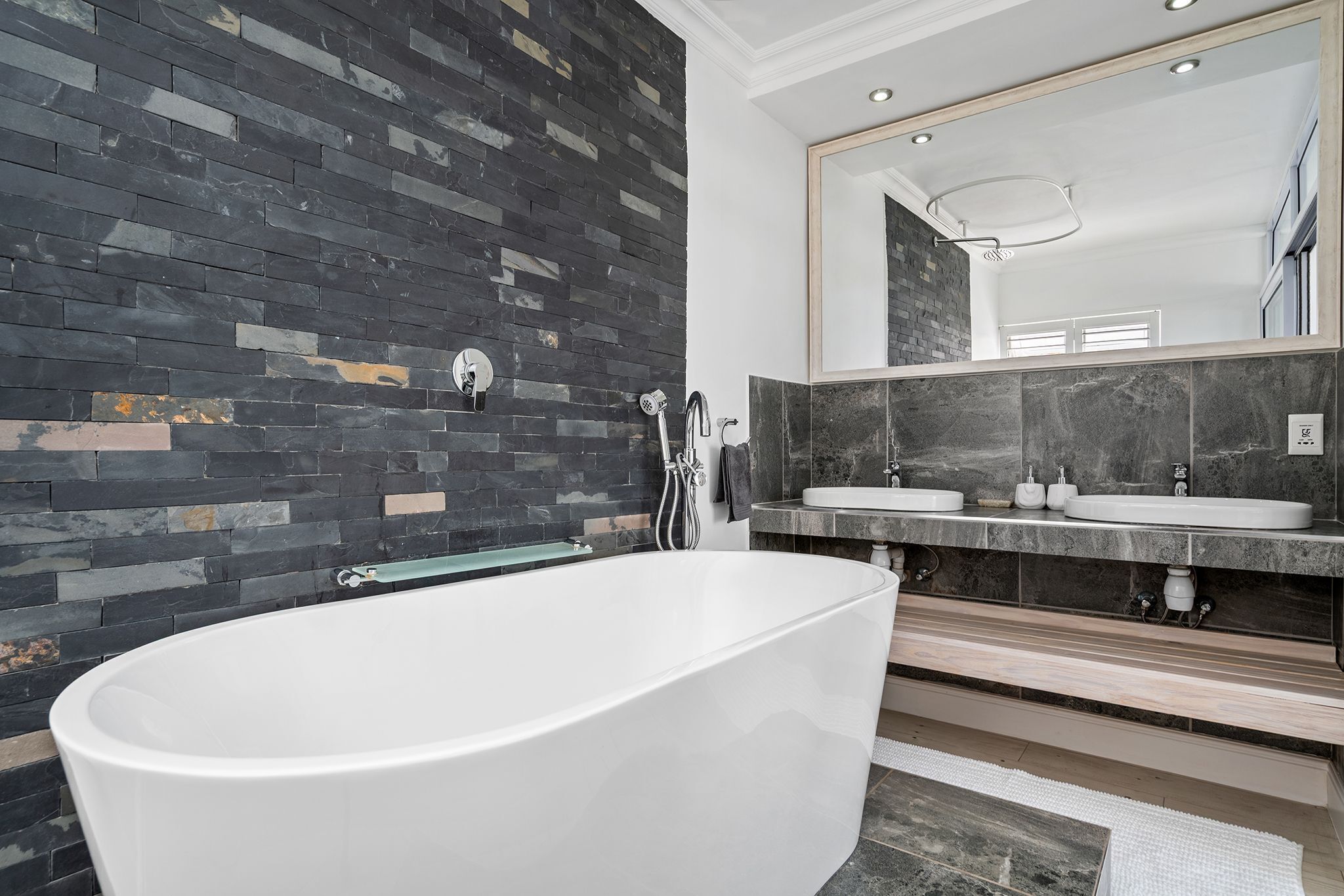 Un baño moderno con una bañera independiente, un espejo grande y un tocador doble.