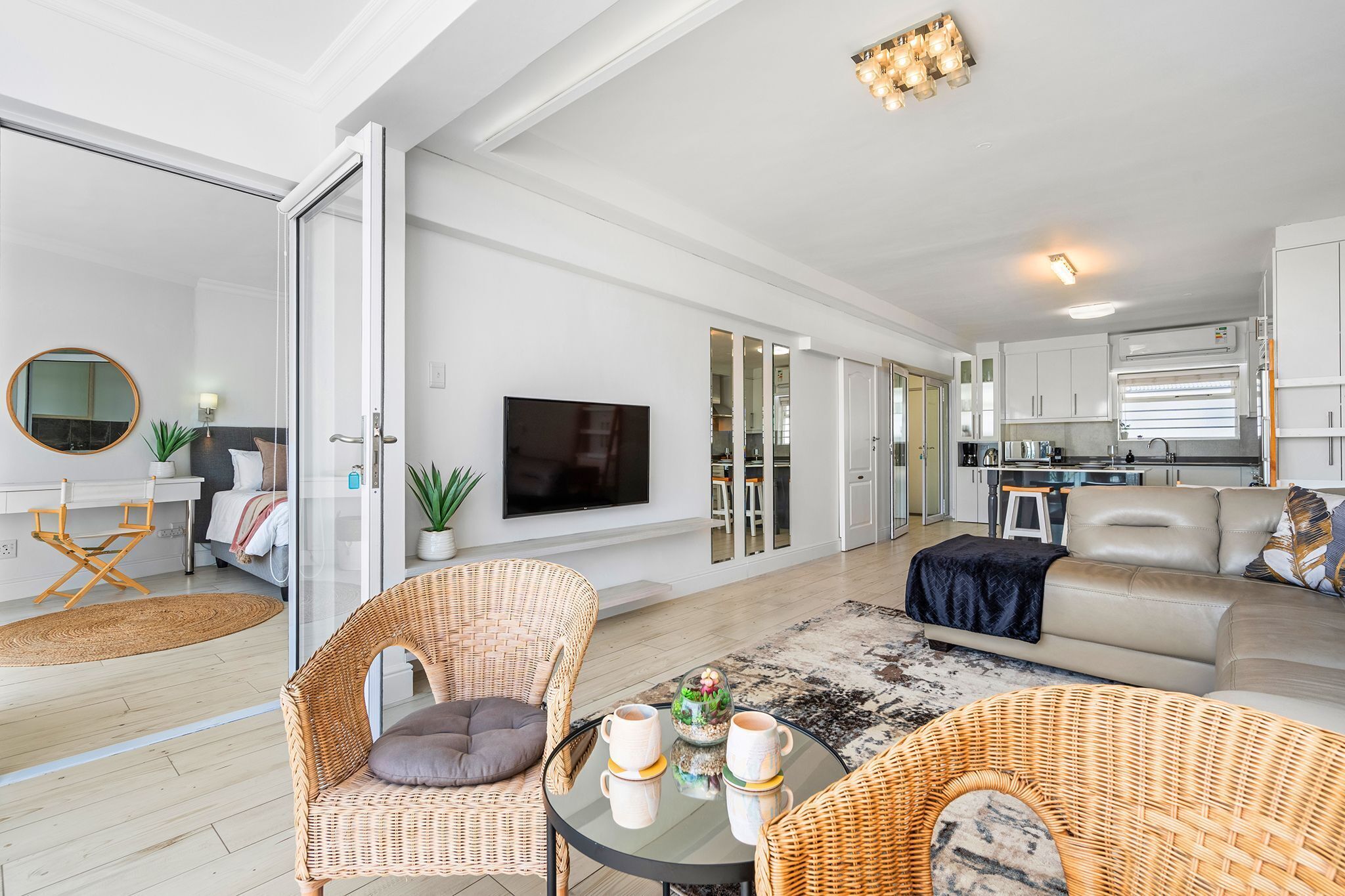 Ein modernes Wohnzimmer mit einer Couch, Korbstühlen, einem Fernseher und einer Küchenzeile.