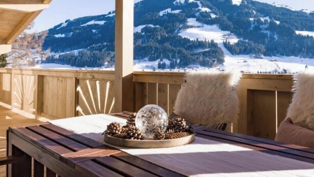 A wooden deck with a table set for two, a snow globe, pine cones, and a mountain view. - Two beautiful apartments in a sunny and quiet location in Westendorf (Salvenberg)