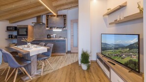 A modern kitchen with built-in appliances, a dining area with a table and chairs, and a television displaying a scenic landscape. - Two beautiful apartments in a sunny and quiet location in Westendorf (Salvenberg)