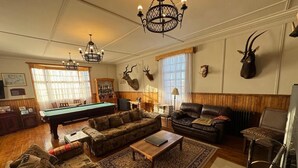 Ein Wohnzimmer mit Billardtisch, Sofas, einem Couchtisch, einer Chandelüster und montierten Tierköpfen.