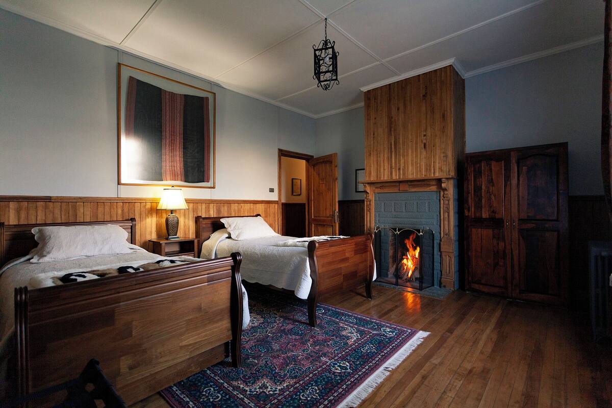 Une chambre de style traditionnel avec deux lits en bois, une cheminée et un grand tapis.