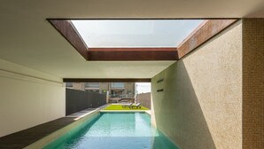 A swimming pool with a skylight, a sun lounger, and a view of buildings in the background. - GuestReady - Luxurious Beachfront Villa Retreat (Vila Nova de Gaia)