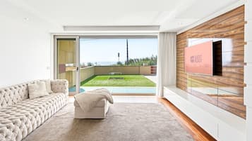 Un salon moderne avec un canapé, un téléviseur fixé sur un mur en bois et une porte-fenêtre coulissante donnant sur un balcon avec vue.