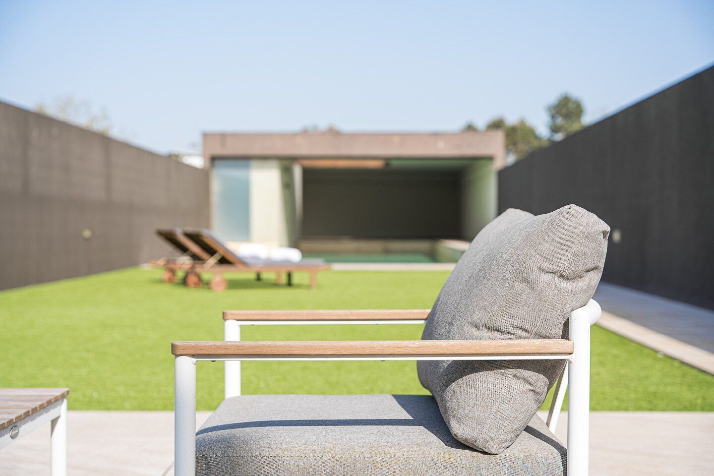 A modern outdoor seating area with a stone backrest chair, a wooden bench, and a poolside lounge chair.