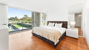 A modern bedroom with a large bed, a bedside table, a mirror, and a balcony with a view of greenery. - GuestReady - Luxurious Beachfront Villa Retreat (Vila Nova de Gaia)