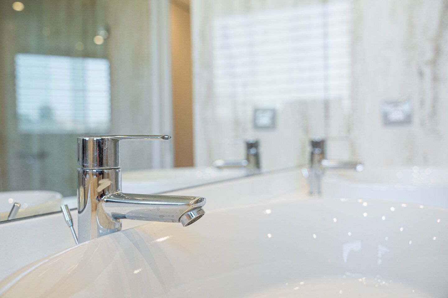 Ein modernes Badezimmer mit großem Spiegel, Chromarmaturen und einem klaren, minimalistischen Design.