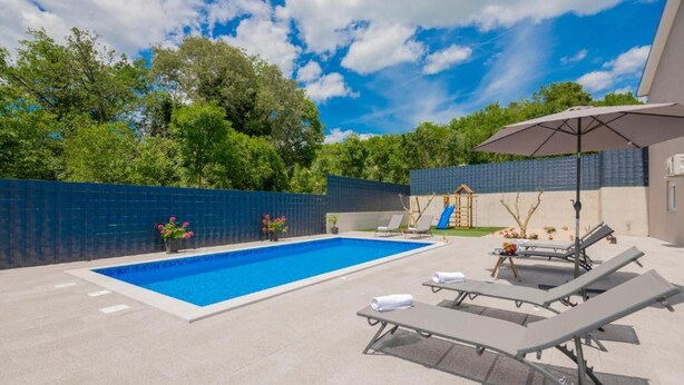 A swimming pool with lounge chairs and a children's play structure. - Vacation home Bozena with pool (Donji Vinjani)