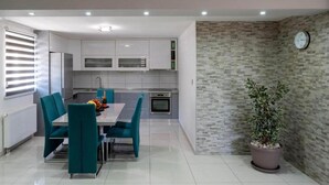 A modern kitchen with white cabinets, a dining table with teal chairs, and a potted plant. - Vacation home Bozena with pool (Donji Vinjani)