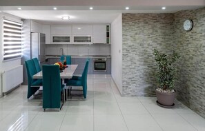 A modern kitchen with white cabinets, a dining table with teal chairs, and a potted plant. - Vacation home Bozena with pool (Donji Vinjani)