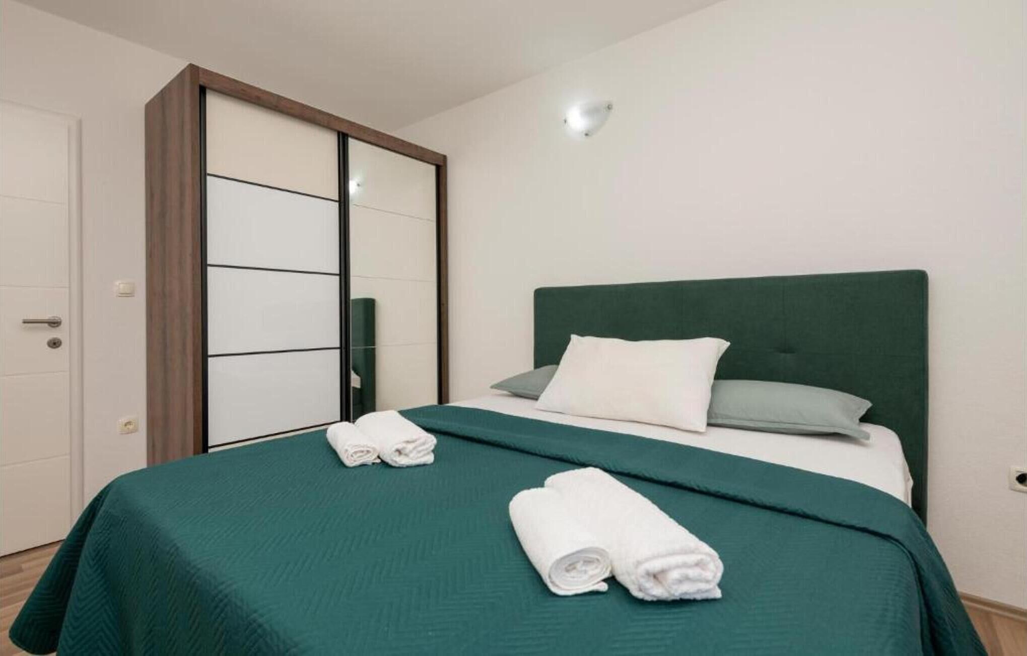 A neatly made bed with a green headboard, white pillows, and rolled white towels.