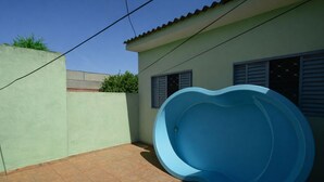 Ein Schwimmbecken mit geschwungener Form, eine geflieste Terrasse und ein Gebäude mit einem gefliesten Dach und Fenstern.