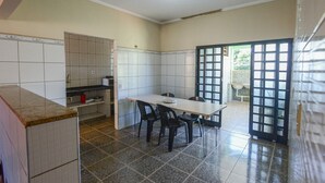 Ein Zimmer mit Fliesenboden, einem Esstisch mit Stühlen, einer Küchenzeile und einer Tür zum Außenbereich.