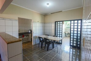A room with a tiled floor, a dining table with chairs, a kitchen area, and a door leading outside.
