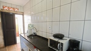 Eine Küche mit weißen Fliesen, einer schwarzen Arbeitsplatte, einem Toaster, einer Kaffeemaschine und einem Fenster mit Jalousien.