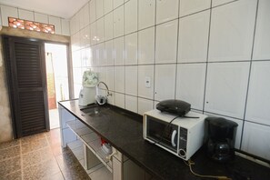 A kitchen with white tiled walls, a black countertop, a toaster, a coffee maker, and a window with blinds.