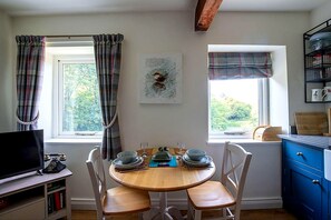 Un coin repas comprenant une table ronde, des chaises, un téléviseur et une fenêtre avec des rideaux.