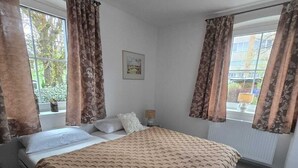 A bedroom with a bed, curtains, a window, a picture on the wall, and a radiator. - Vacation apartment with several living units (up to 20 people) (Wunsiedel)