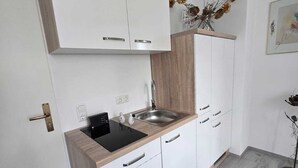 A modern kitchen with white cabinets, a wooden countertop, a sink, and a black induction cooktop. - Vacation apartment with several living units (up to 20 people) (Wunsiedel)
