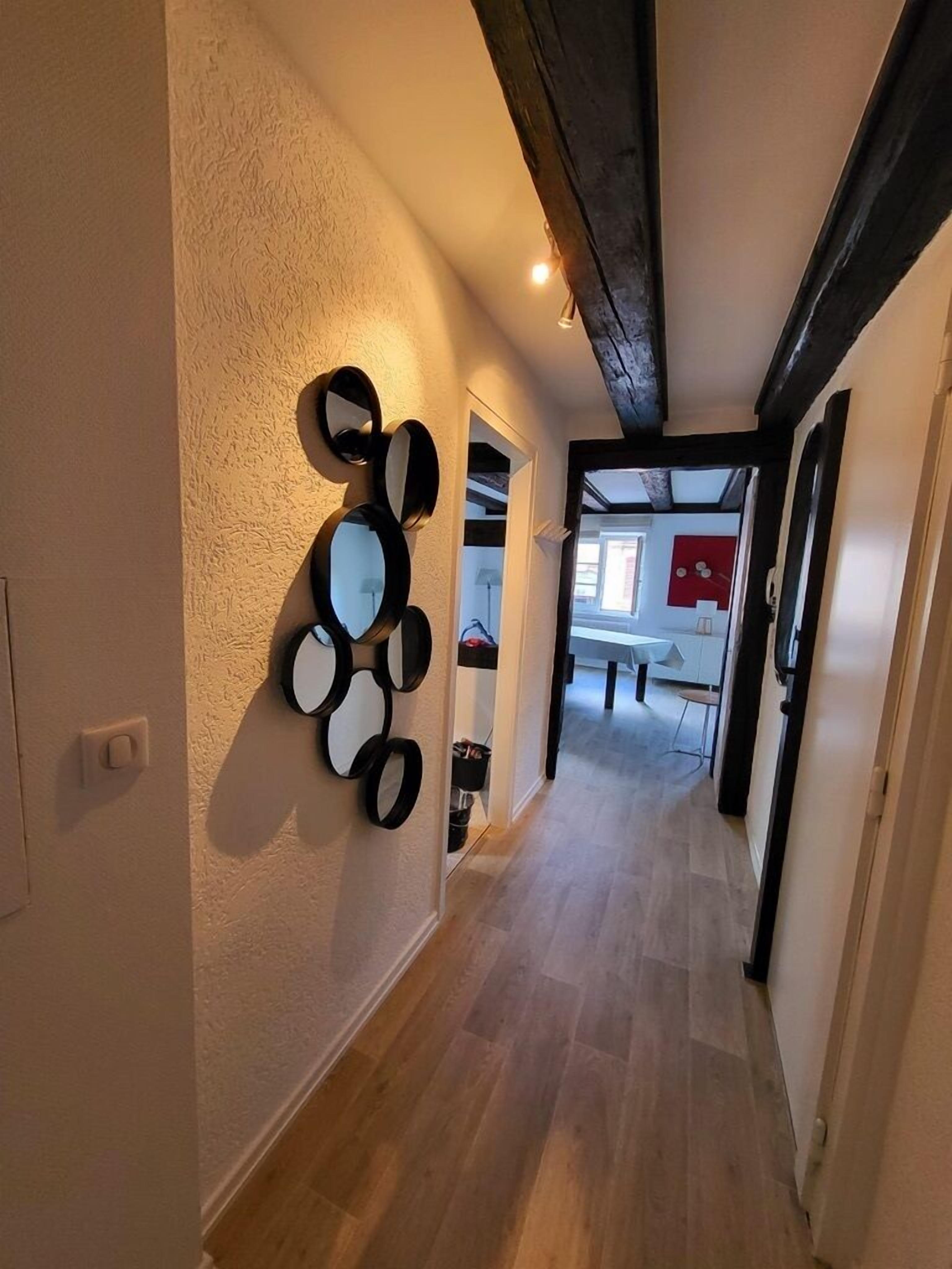 Un couloir doté d’un plancher en bois, d’un ensemble de miroirs fixés au mur et d’une porte donnant sur une autre pièce.
