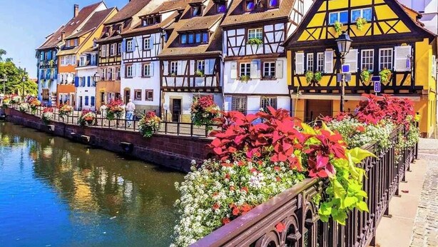 Une rangée de maisons aux façades colorées, à pans de bois, bordant un canal.