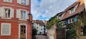 A narrow street with buildings on either side, featuring traditional architecture and shutters. - LARGE 2-BEDROOM APARTMENT OVERLOOKING PETITE VENISE WITH BALCONY AND PRIVATE PARKING (Colmar)