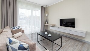 A modern living room with a sofa, a coffee table, a TV mounted on a wall, and a window with curtains. - BelMare Aqua Resort 233 by Solarento (Międzyzdroje)