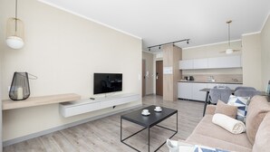 A modern living room with a flat-screen TV, a coffee table, a sofa, and a kitchen in the background. - BelMare Aqua Resort 233 by Solarento (Międzyzdroje)