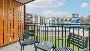 A balcony with a view of a playground, a pool, and a building with a distinctive roof. - BelMare Aqua Resort 233 by Solarento (Międzyzdroje)