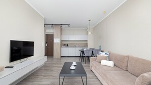 A modern living room with a flat-screen TV, a coffee table, a sofa, and a kitchen in the background. - BelMare Aqua Resort 233 by Solarento (Międzyzdroje)