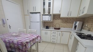 Uma cozinha compacta com armários brancos, geladeira, micro-ondas e fogão a gás.